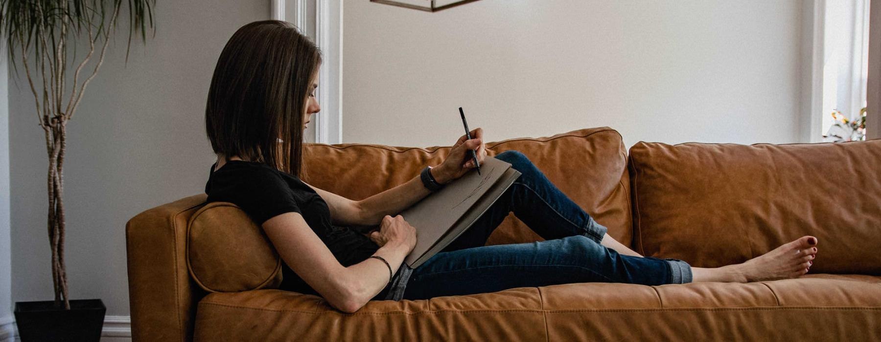 woman lies on a couch and draws on a large sketch pad